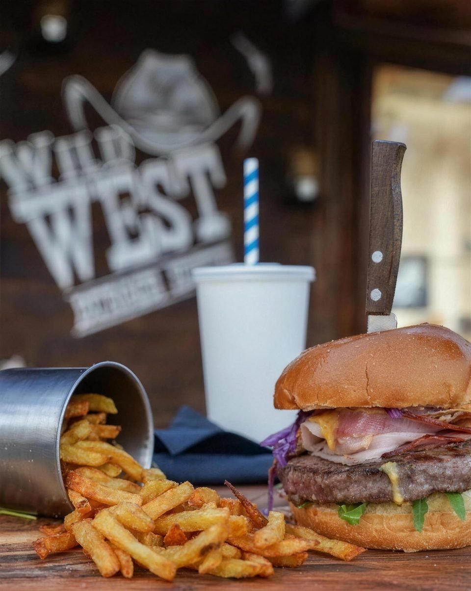 Burger i pomfrit u metalnoj čaši ispred zidnog natpisa Wild West